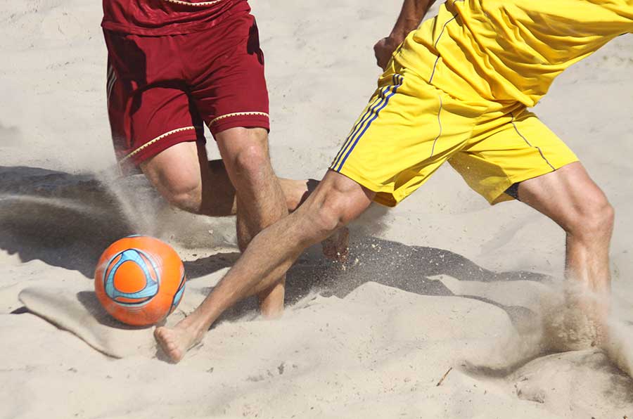 Nahaufnahme von zwei Strandfußballern im Zweikampf um den Ball